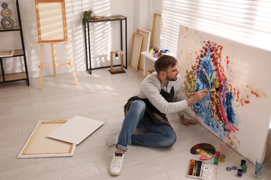 Photo of Young man painting on canvas with brush in artist studio