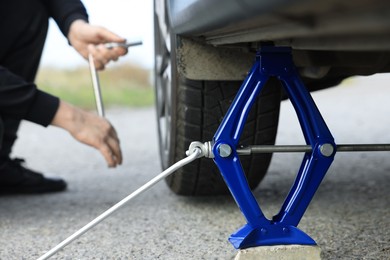 Photo of Man changing car tire, focus on scissor jack outdoors