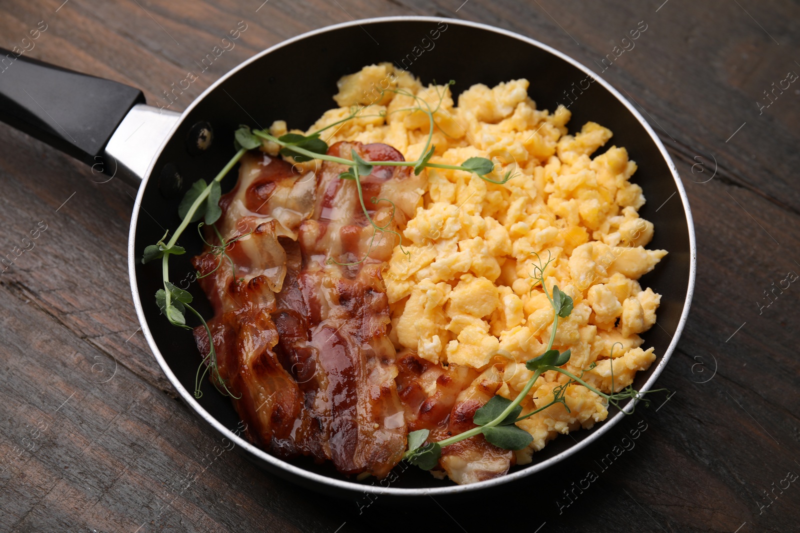 Photo of Delicious scrambled eggs with bacon in frying pan on wooden table