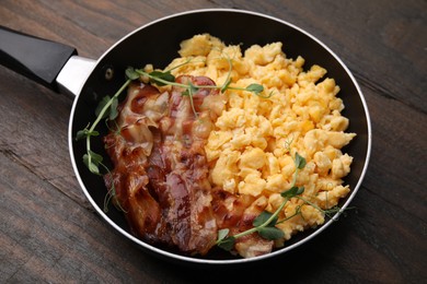 Delicious scrambled eggs with bacon in frying pan on wooden table