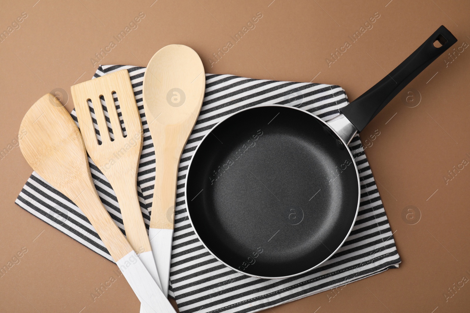 Photo of Different kitchen utensils, napkin and frying pan on light brown background, flat lay