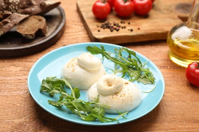 Photo of Delicious burrata cheese with arugula on wooden table