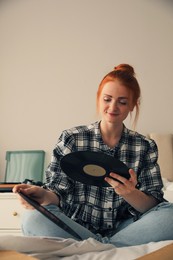 Young woman choosing vinyl disc to play music with turntable in bedroom