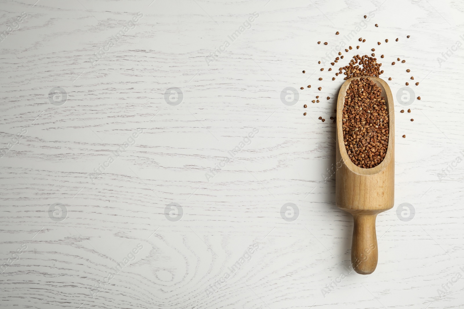 Photo of Buckwheat grains on white wooden table, top view. Space for text