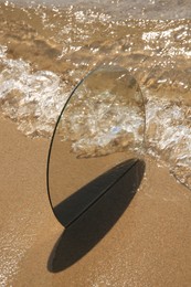 Round mirror reflecting sea on sandy beach