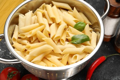 Photo of Cooked pasta in metal colander and chili on dark textured table, closeup