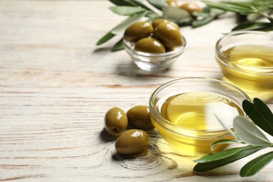 Photo of Bowls with cooking oil, olives and green leaves on white wooden table. Space for text