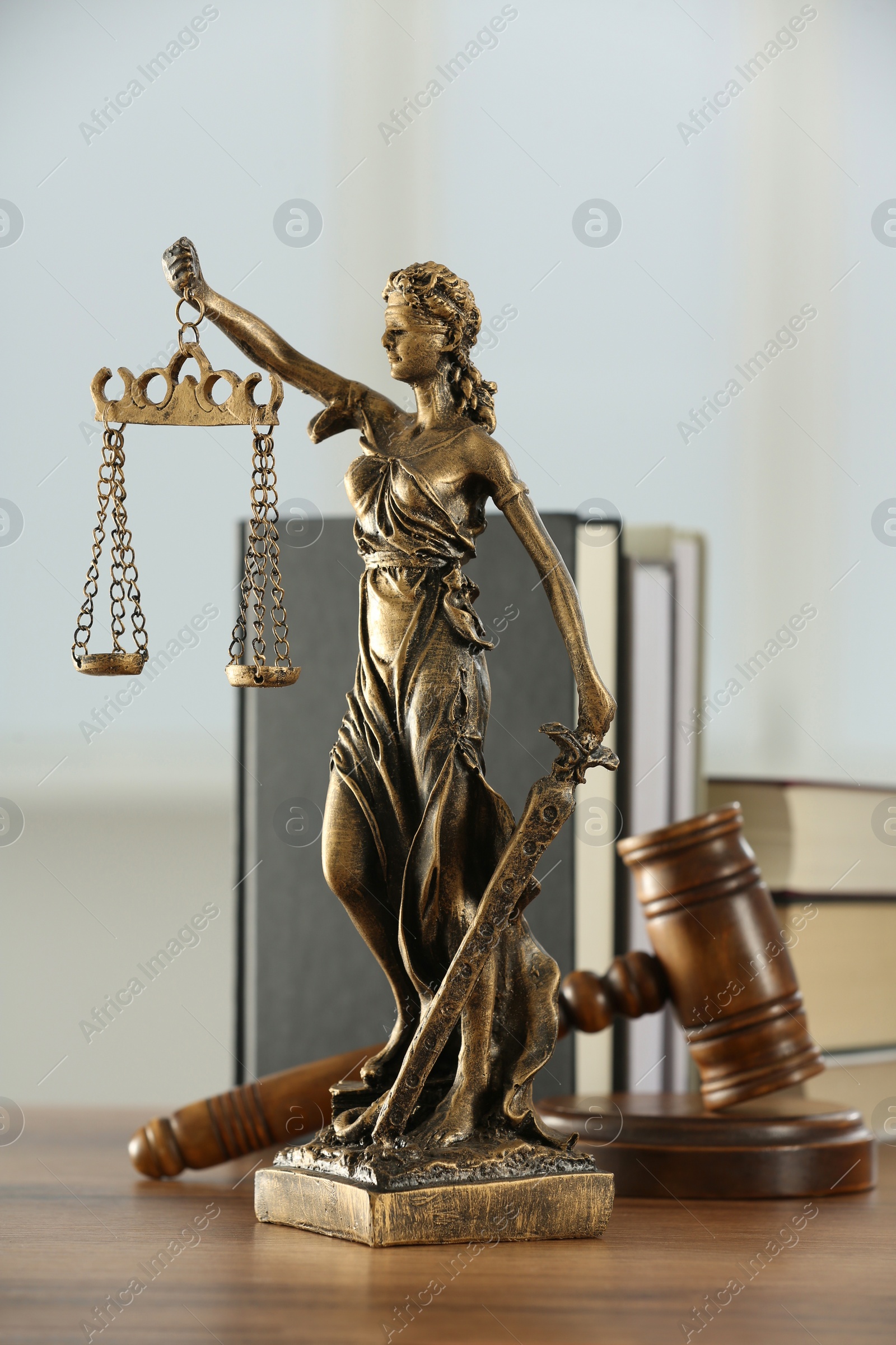 Photo of Figure of Lady Justice, gavel and books on wooden table indoors. Symbol of fair treatment under law