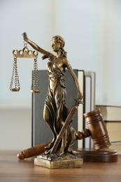 Figure of Lady Justice, gavel and books on wooden table indoors. Symbol of fair treatment under law