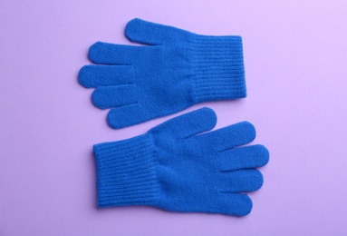 Pair of stylish woolen gloves on violet background, flat lay