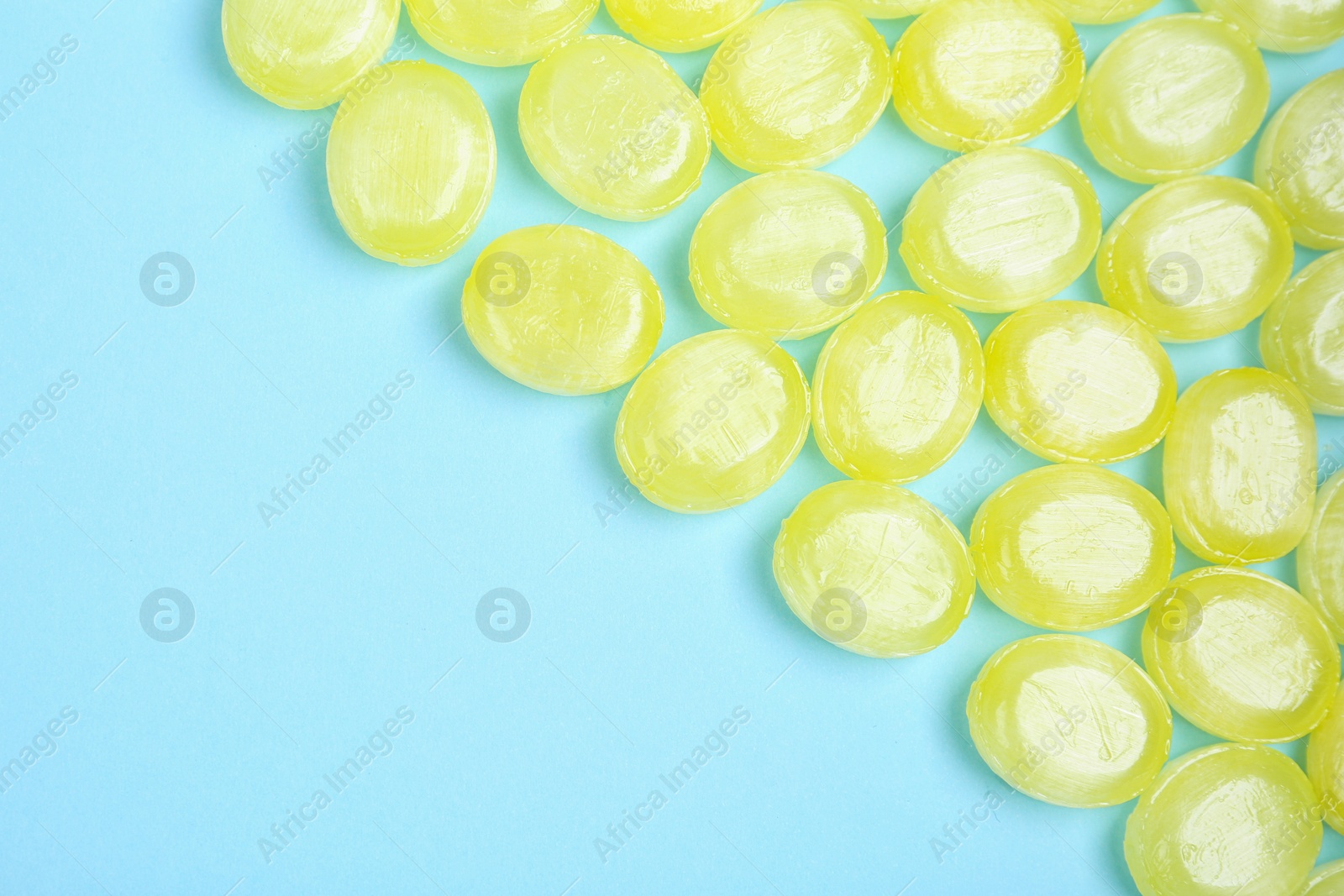 Photo of Many delicious lemon drops on light blue background, flat lay. Space for text