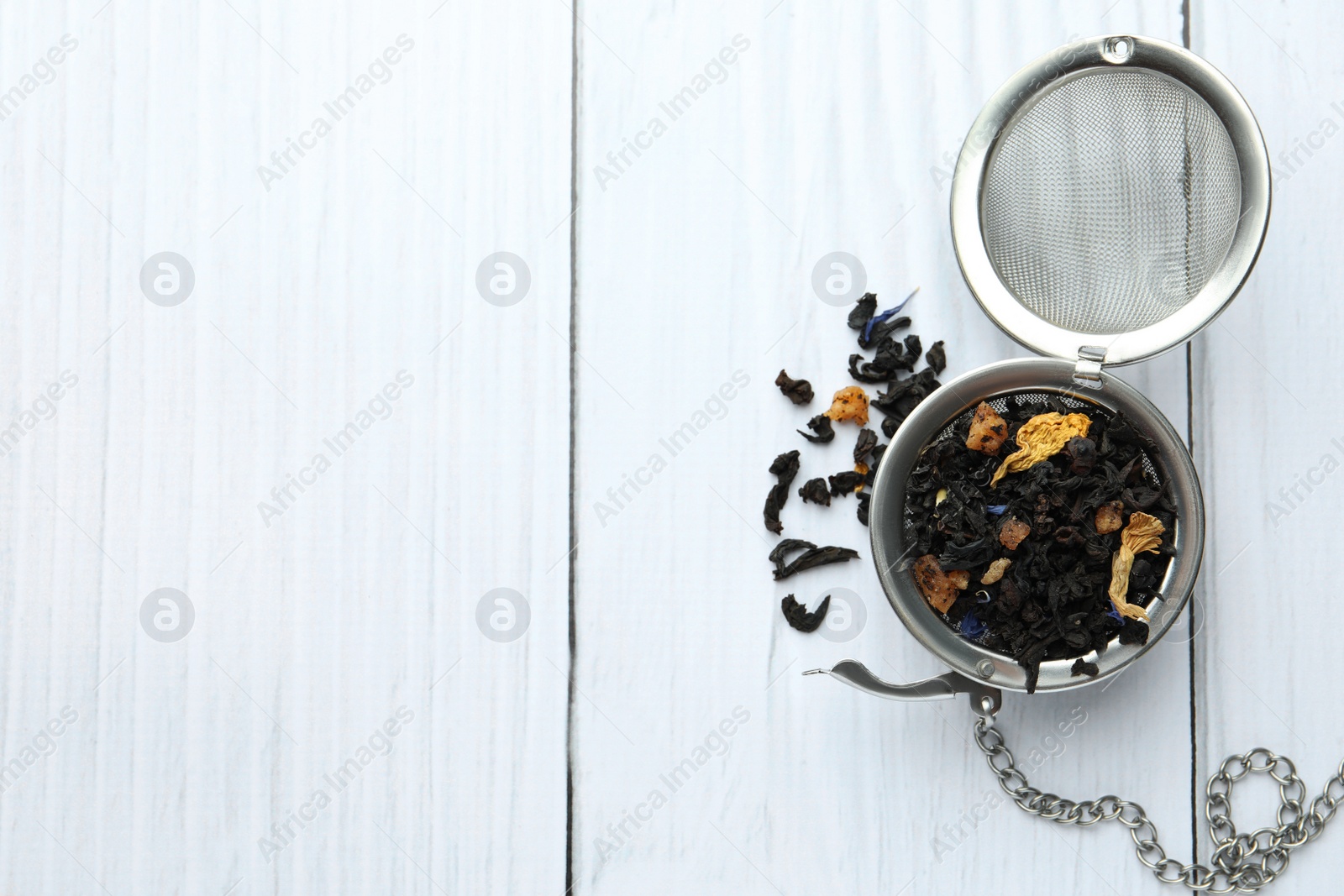 Photo of Snap infuser with dried herbal tea leaves on white wooden table, top view. Space for text