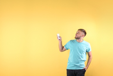 Young man with air conditioner remote on color background, copy space text