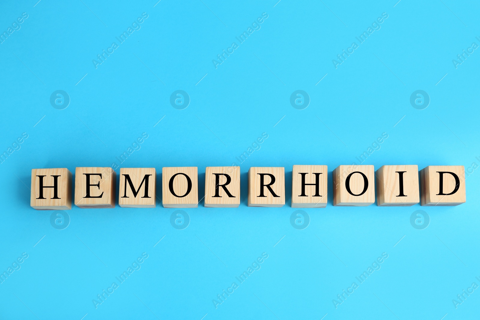 Photo of Wooden cubes with word HEMORRHOID on light blue, top view