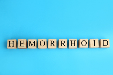 Wooden cubes with word HEMORRHOID on light blue, top view