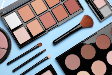 Photo of Different contouring palettes and brushes on light blue background, flat lay. Professional cosmetic product