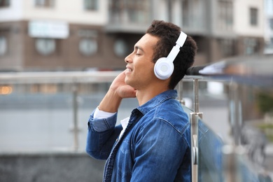 Handsome young African-American man with headphones listening to music on city street