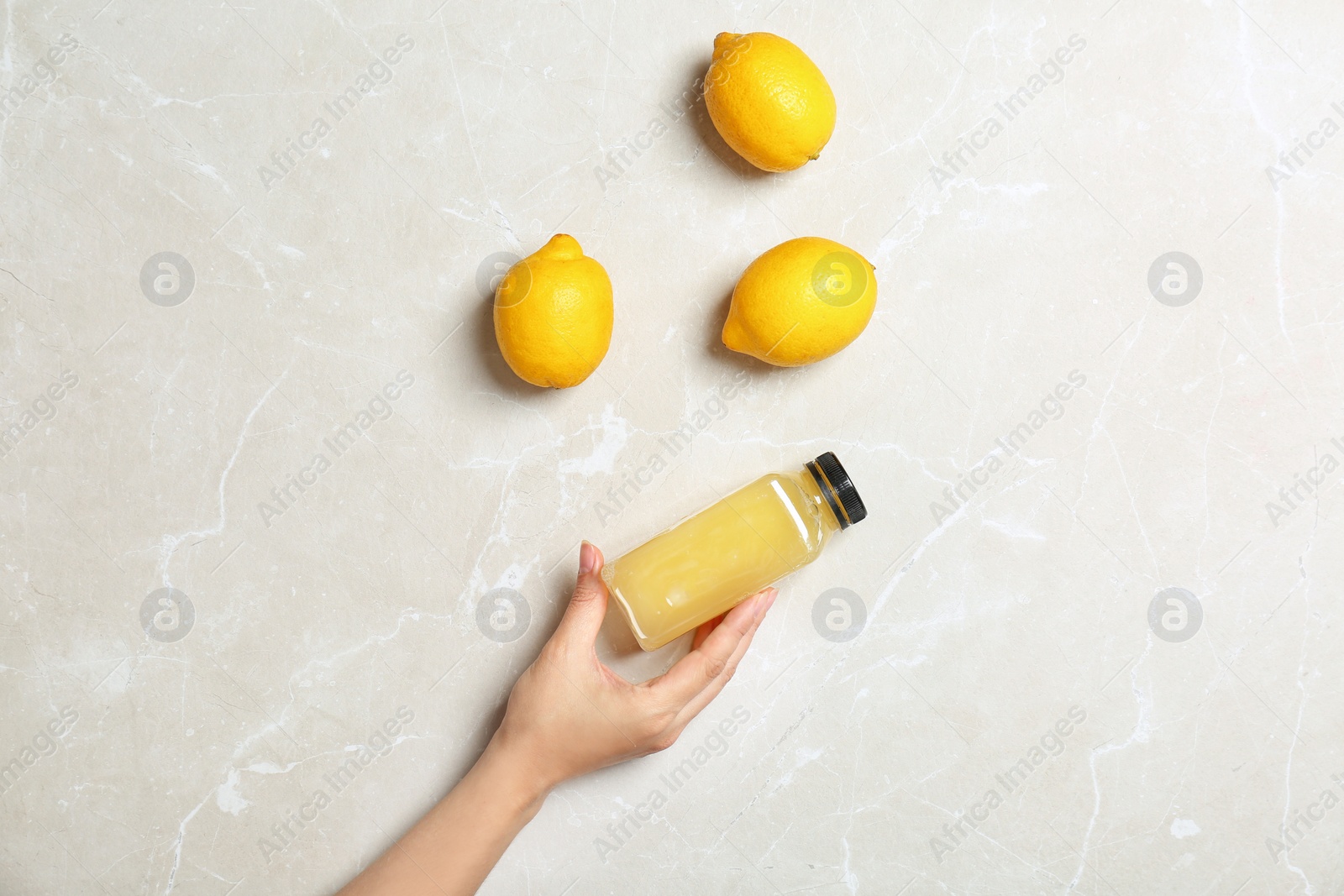 Photo of Woman holding bottle with fresh juice near lemons on light background, top view