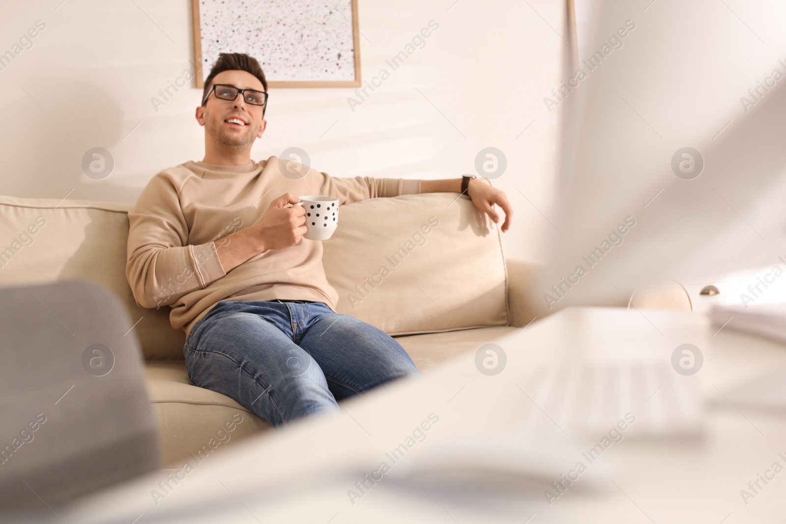 Photo of Young man with cup of drink relaxing on couch in office during break