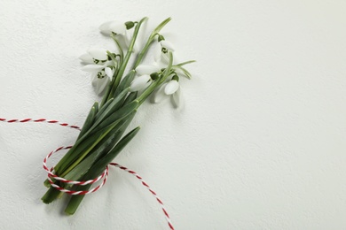 Beautiful snowdrops with traditional cord martisor on white background, flat lay and space for text. Symbol of first spring day