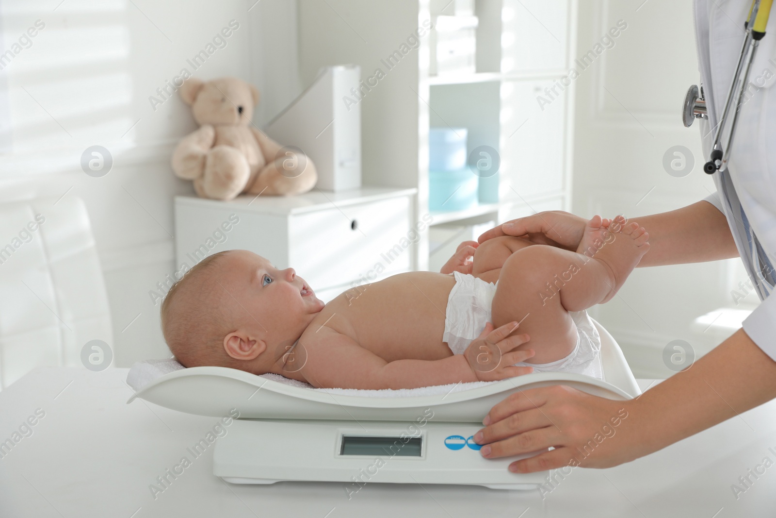 Photo of Pediatrician weighting cute baby in clinic, closeup. Health care