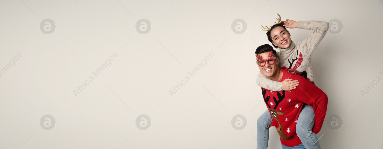 Photo of Couple in Christmas sweaters, deer headband and party glasses on white background, space for text