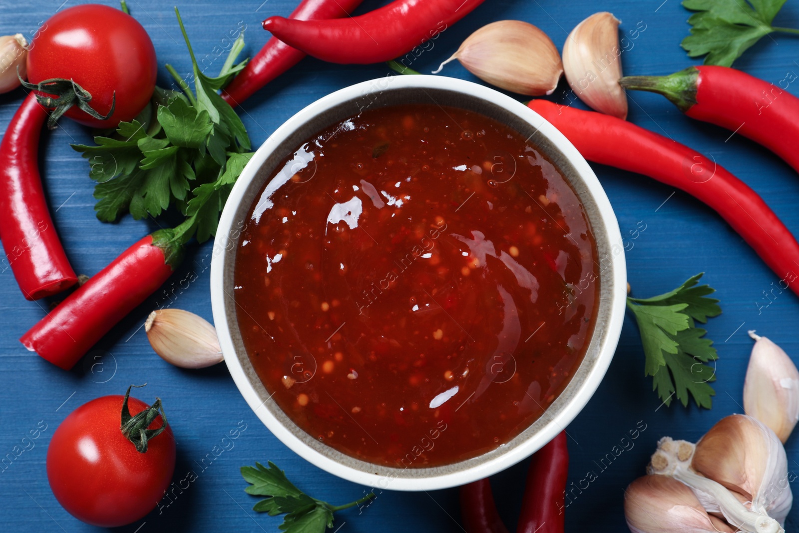 Photo of Spicy chili sauce and ingredients on blue wooden table, flat lay