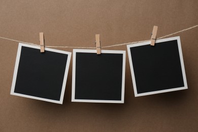 Photo of Wooden clothespins with empty instant frames on twine against brown background. Space for text