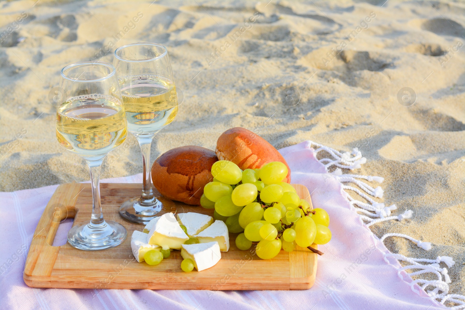 Photo of Glasses with white wine and snacks on beach sand outdoors. Space for text