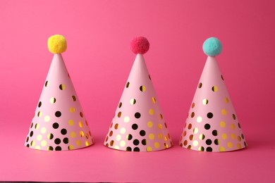 Photo of Beautiful party hats with pompoms on pink background