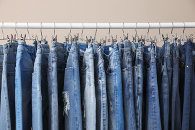 Photo of Rack with stylish jeans on beige background, closeup