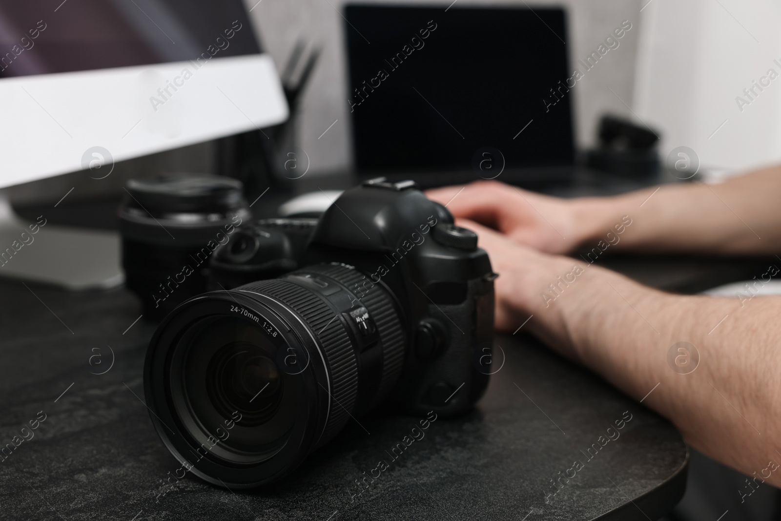 Photo of Camera on dark table, closeup. Photographer working with computer indoors, selective focus