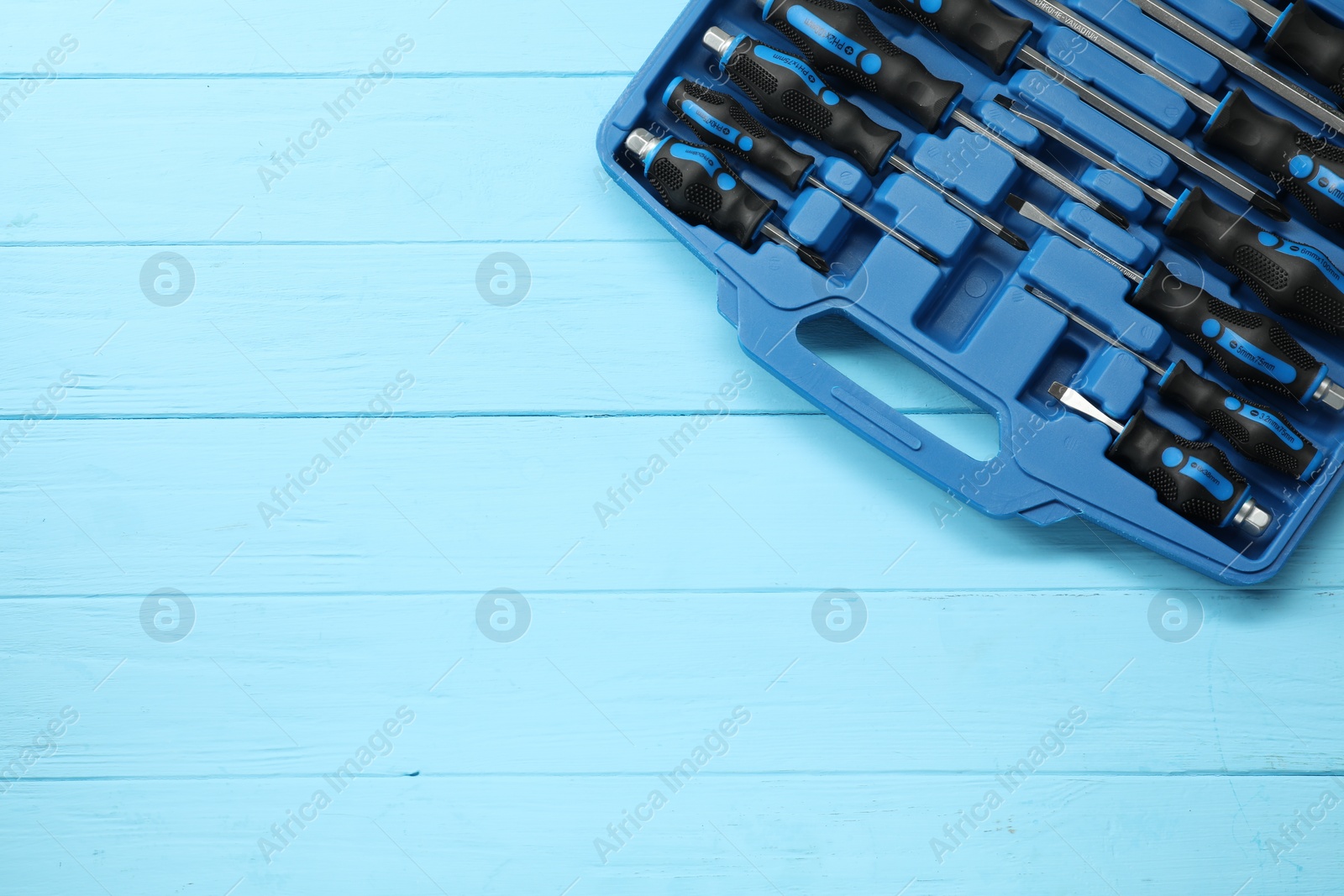 Photo of Set of screwdrivers in open toolbox on light blue wooden table, top view. Space for text