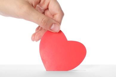 Photo of Woman putting red heart into slot of donation box against white background, closeup