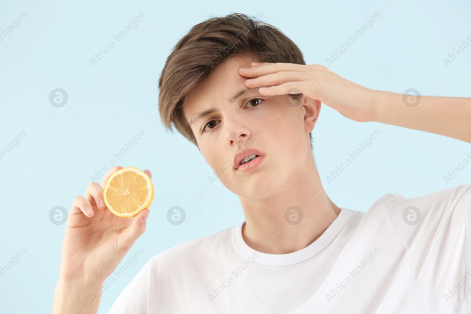 Photo of Teenage boy with acne problem holding lemon on light background. Skin allergy