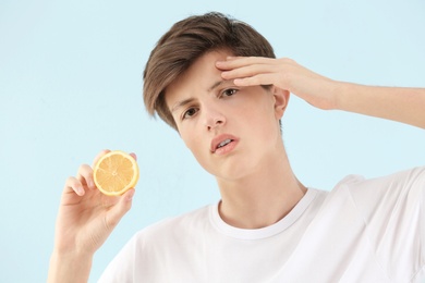 Teenage boy with acne problem holding lemon on light background. Skin allergy