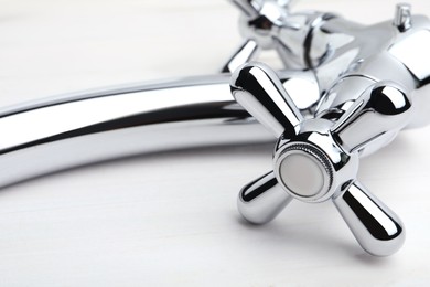 Photo of Double handle water tap on white wooden table, closeup