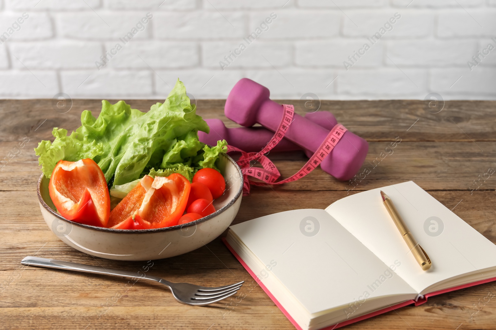 Photo of Healthy diet. Vegetables, fork, notebook, dumbbells and measuring tape on wooden table