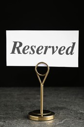Photo of Elegant sign RESERVED on grey surface. Table setting element