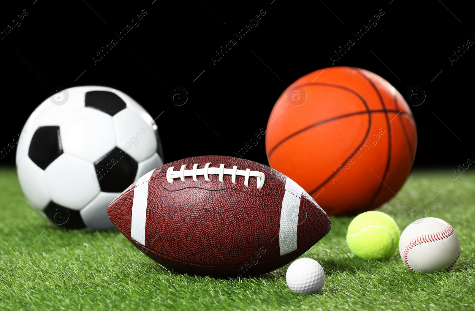 Photo of Many different sports balls on green grass against black background