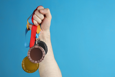 Photo of Man holding medals on blue background, closeup. Space for design