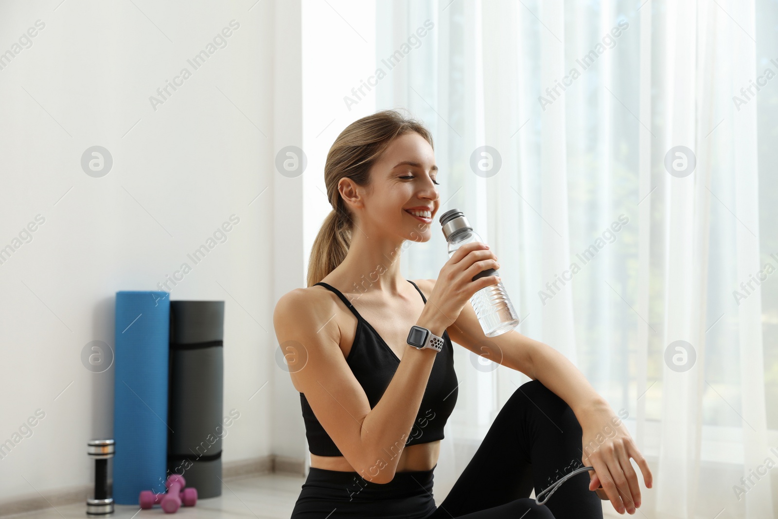 Photo of Young woman with modern smart watch drinking water indoors