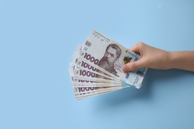 Photo of Woman holding Ukrainian money on light blue background, closeup