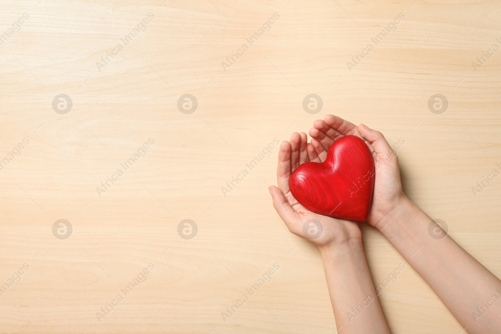 Photo of Woman holding heart on wooden background, top view with space for text. Donation concept