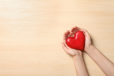 Woman holding heart on wooden background, top view with space for text. Donation concept