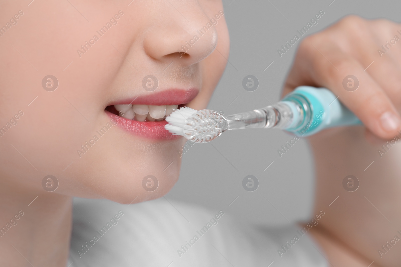 Photo of Girl brushing her teeth with electric toothbrush on light grey background, closeup