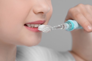 Girl brushing her teeth with electric toothbrush on light grey background, closeup
