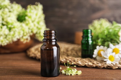Photo of Bottle of essential oil with flowers on wooden table, space for text
