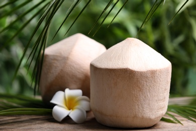Photo of Young peeled coconuts with palm leaf and flower on wooden table
