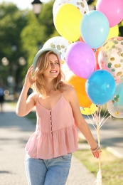 Young woman with colorful balloons outdoors on sunny day